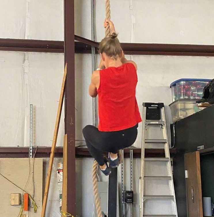 Female climbing a rope in gym to improve physical health